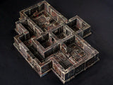 A miniature dungeon terrain set featuring interconnected stone rooms and corridors. The structure is painted in dark grey and reddish-brown tones with a weathered, textured finish, including square floor tiles and raised wall segments.