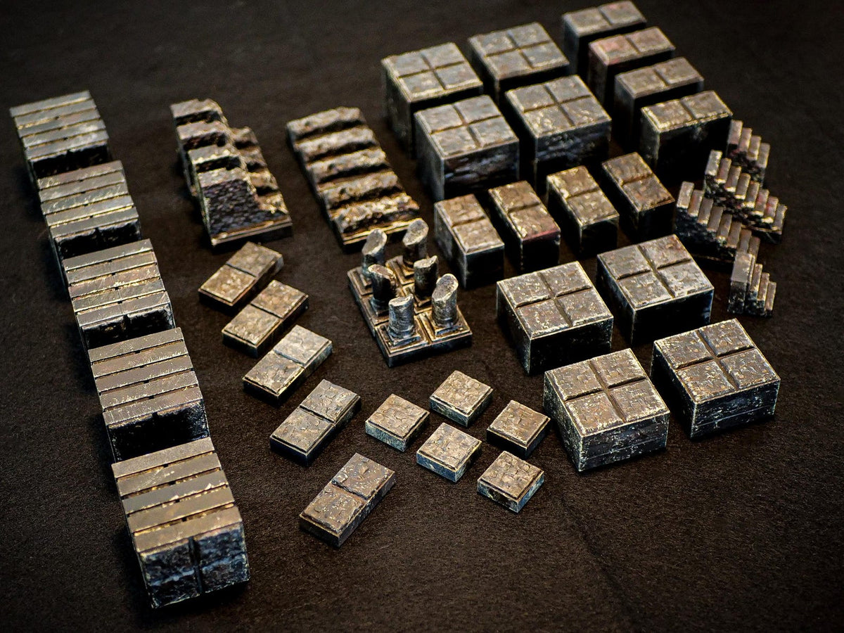 A collection of dark, weathered stone-like miniature terrain pieces for tabletop gaming. The set includes various square blocks, rectangular tiles, small staircases, and a central platform with four short, cylindrical pillars.