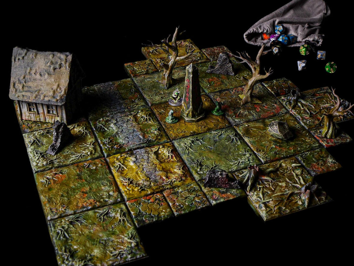 A tabletop gaming terrain set featuring modular square tiles with a swampy, textured green and brown landscape. The set includes a small cottage, a central stone obelisk with red markings, bare tree models, rocks, and a cloth dice bag.