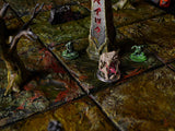 A tabletop gaming terrain set featuring a grid of textured, mossy green and brown tiles. The scene includes a tall, weathered stone obelisk with red carved symbols, a bare tree, and several small, painted monster miniatures.