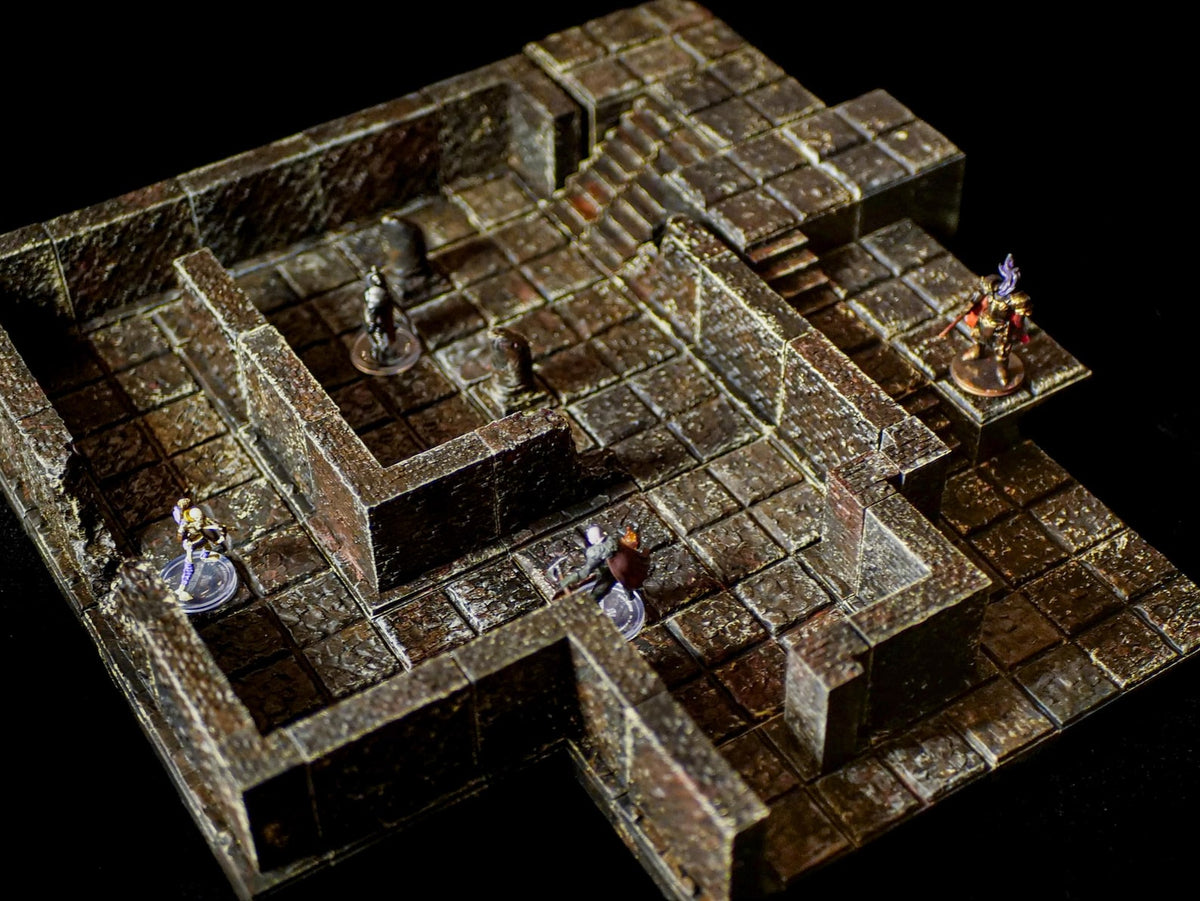 A modular tabletop dungeon terrain set featuring dark brown stone-textured floor tiles and walls. The layout includes a raised platform, a staircase, and several small miniature figures positioned within the grid-based stone corridors.