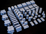 A collection of light blue miniature dungeon terrain pieces, including square floor tiles with grid patterns, various wall segments with stone textures, staircases, and pillar components, all designed for tabletop gaming setups.