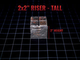 A square riser with a dark, weathered stone-like texture and a cross-shaped groove on the top surface. The text 2x2 RISER - TALL is displayed above the object, and 2 HEIGHT is indicated next to the side with a red measurement line.