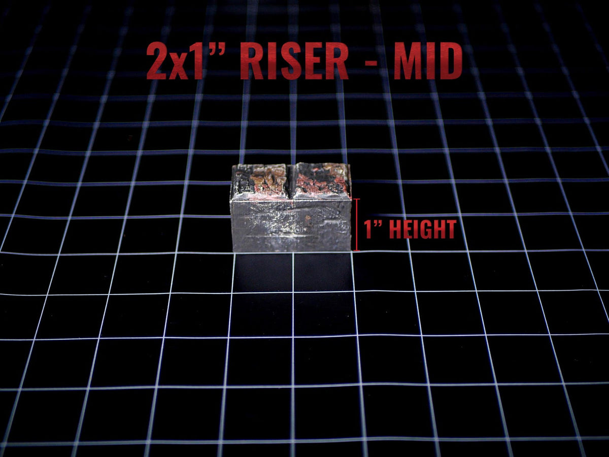 A rectangular metal riser with a weathered, dark grey finish and a central vertical groove. The object is labeled with the text 2x1" RISER - MID and features a red indicator line showing a 1" height measurement on the side.