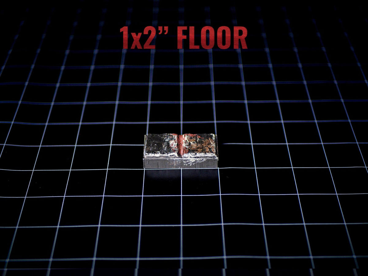 A rectangular 1x2 inch floor tile piece with a metallic silver finish and a dark, weathered, or burnt texture on the top surface. The object is positioned on a black grid background with the text 1x2 inch FLOOR printed above it.