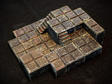 A modular tabletop gaming terrain piece featuring a multi-level stone floor design with integrated stairs. The structure is composed of dark, weathered square tiles with a textured, metallic finish and visible bronze-toned highlights.