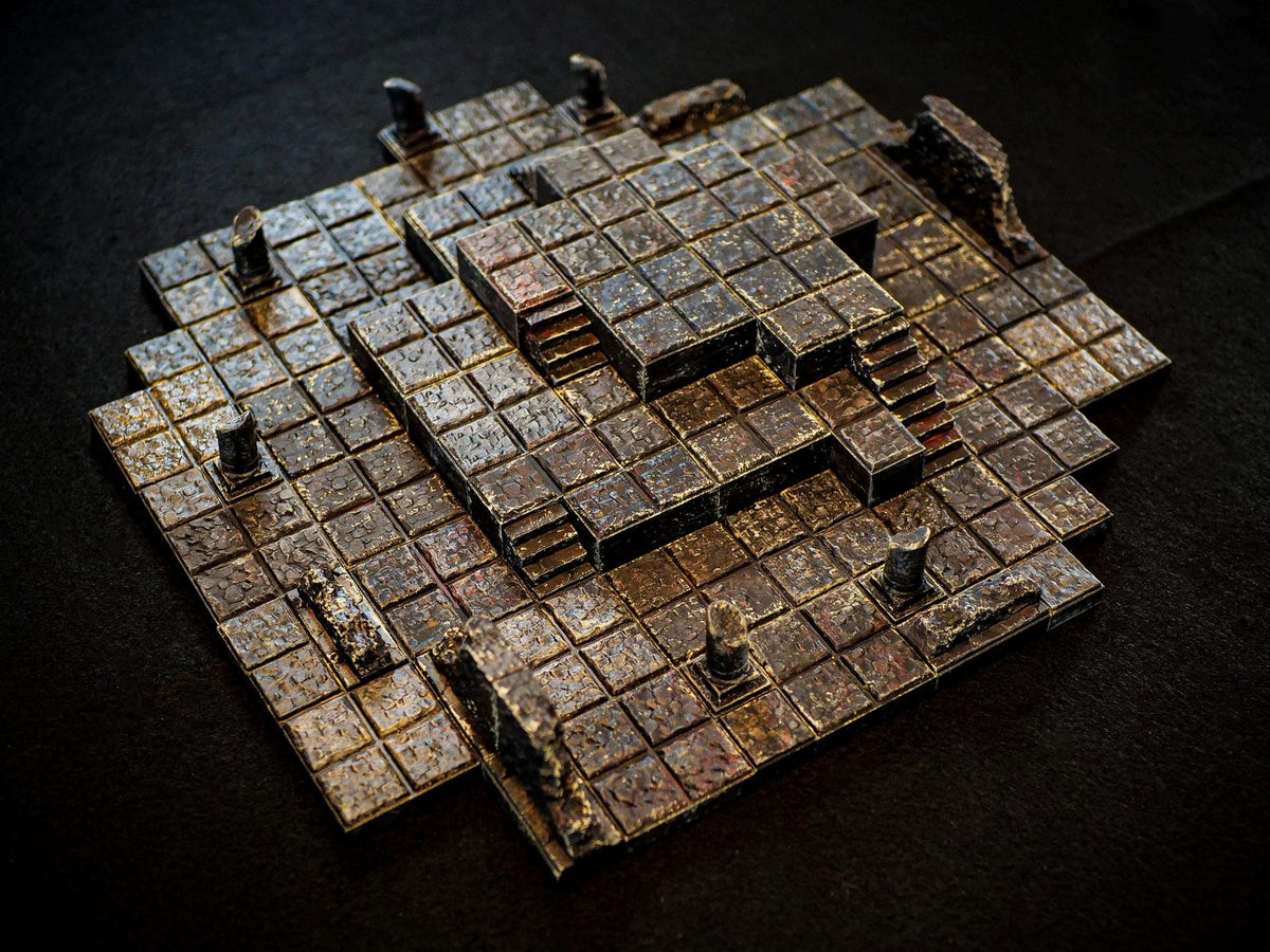 A multi-level dungeon terrain tile set featuring a grid of square stone blocks with a weathered, dark brown and metallic finish. The structure includes raised platforms, small staircases, and broken pillar fragments arranged in a layout.