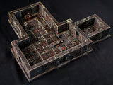 A miniature dungeon room terrain piece featuring dark, weathered stone walls and a grid-patterned floor with reddish-brown highlights. The structure includes an open layout with a small altar, a pillar, and a gated archway entrance.