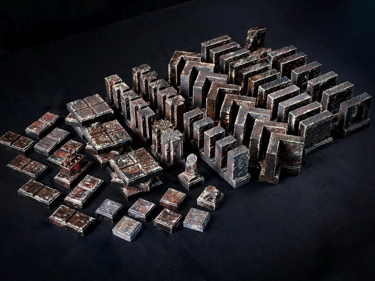 A collection of dark, weathered, metallic-looking modular dungeon tiles and wall segments. The pieces feature a textured, distressed finish with shades of charcoal, rust, and bronze, arranged in various geometric shapes and sizes.