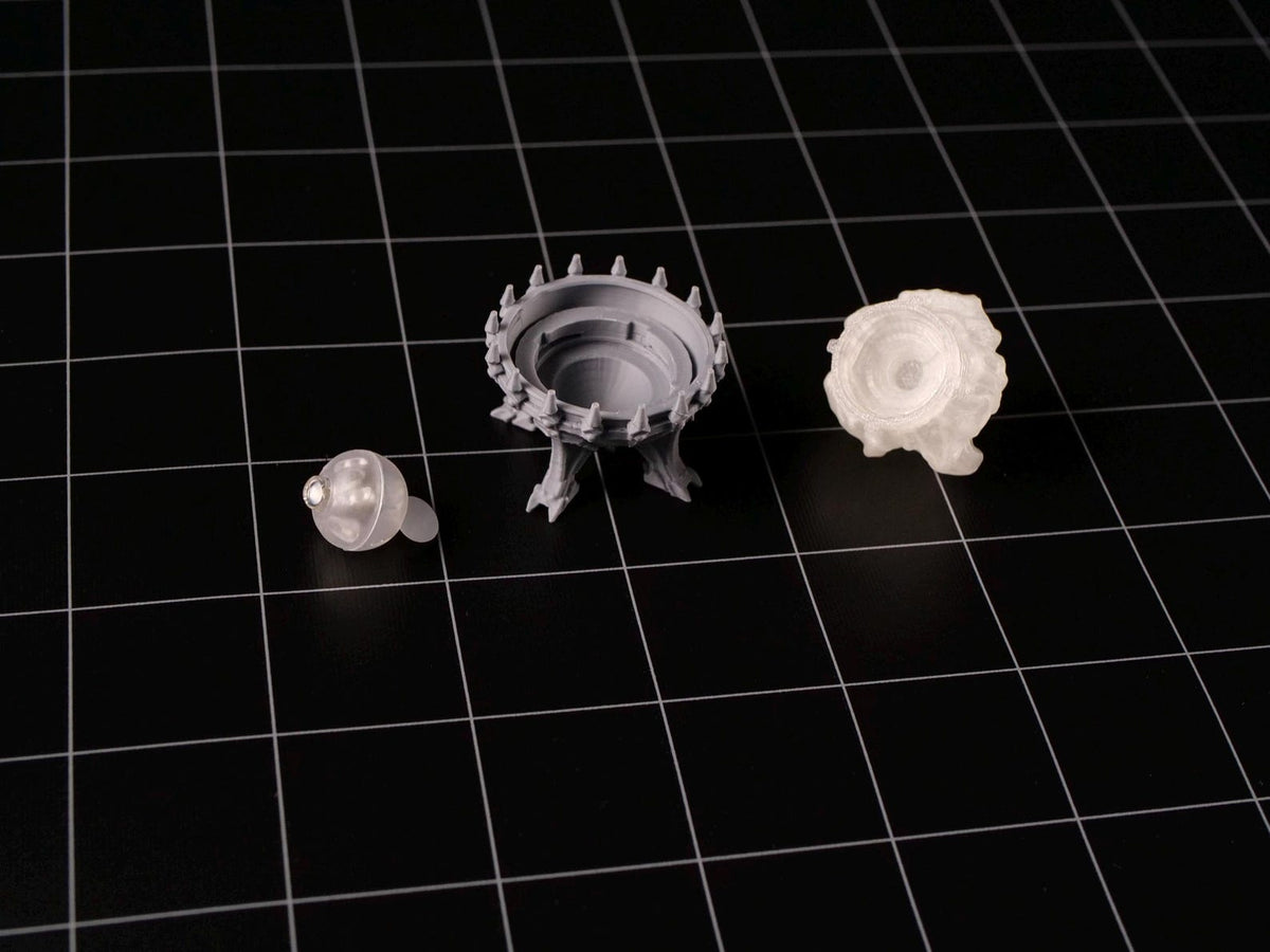 Three unpainted gray resin miniature components consisting of a small spherical orb, a circular basin with spiked edges supported by three legs, and a textured, cloud-like base piece, all displayed as separate parts for assembly.