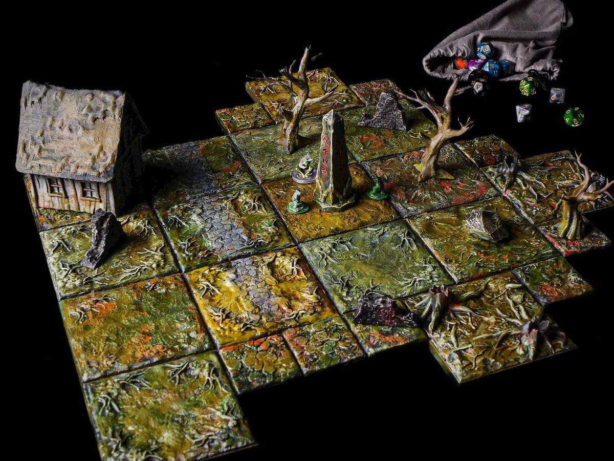 A tabletop gaming terrain set featuring modular square tiles with a swampy, overgrown texture in shades of green and brown. The set includes a small house, a central stone obelisk with red markings, bare trees, rocks, and a cloth dice bag.