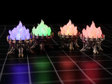 Four miniature metal-colored braziers with spiked rims, each containing a translucent flame-shaped insert. The flames are illuminated in blue, green, orange, and pink, casting a glow on the dark surface beneath the objects.