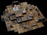A multi-level dungeon terrain set featuring a dark, weathered stone tile grid with raised platforms, staircases, and broken pillar ruins. Four miniature figures on clear circular bases are positioned across the modular stone layout.