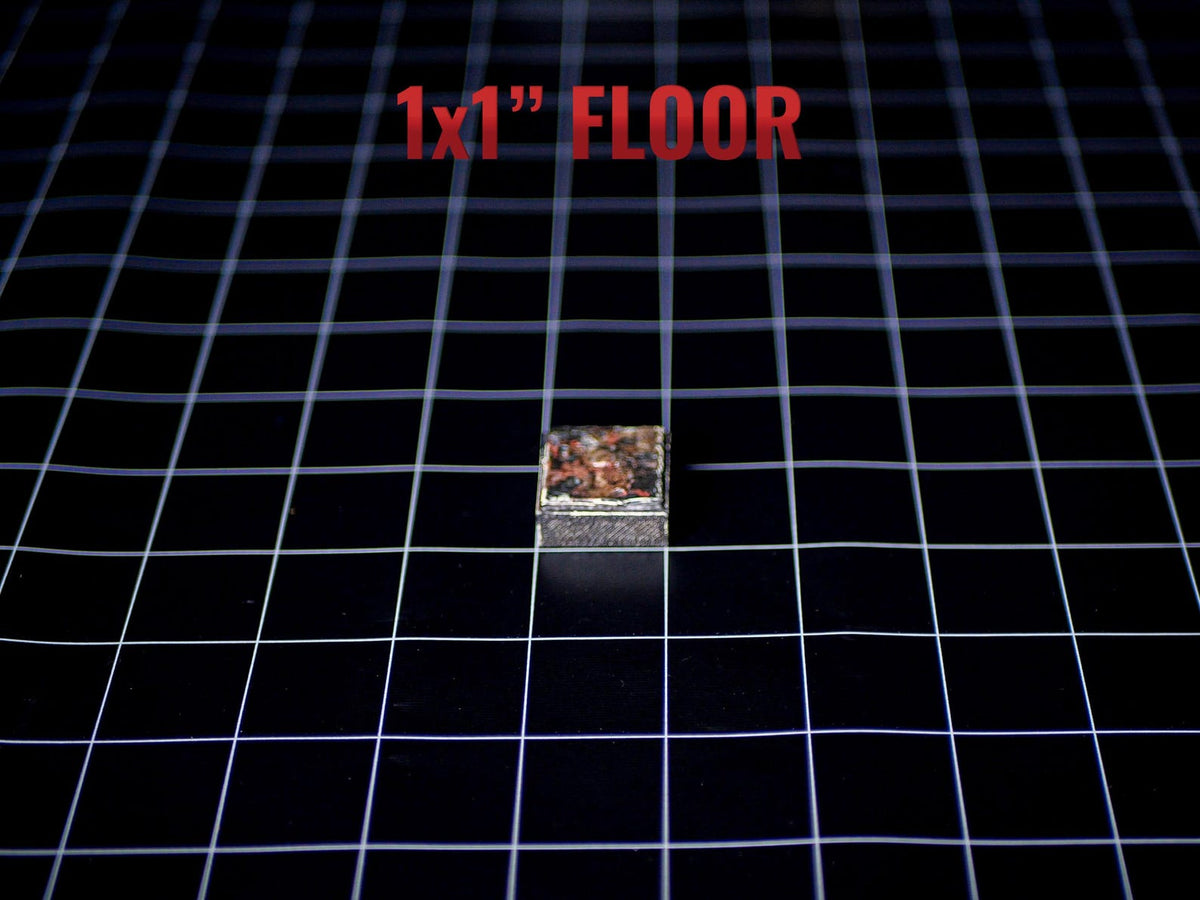 A small square tile measuring 1x1 inch with a textured, multi-colored surface featuring shades of brown, black, and metallic tones. The tile is positioned on a black grid background with the red text 1x1" FLOOR printed above it.