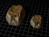 Two textured, irregular, mound-shaped terrain pieces with a layered, topographical appearance. The surfaces feature a mottled color palette of earthy browns, greens, and reddish-orange tones, with visible ridges and recessed areas.