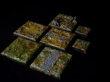 A collection of seven square and rectangular terrain tiles featuring textured surfaces in shades of green, brown, and grey. The tiles display raised details including tree stumps, root systems, and stone pathways with a glossy finish.