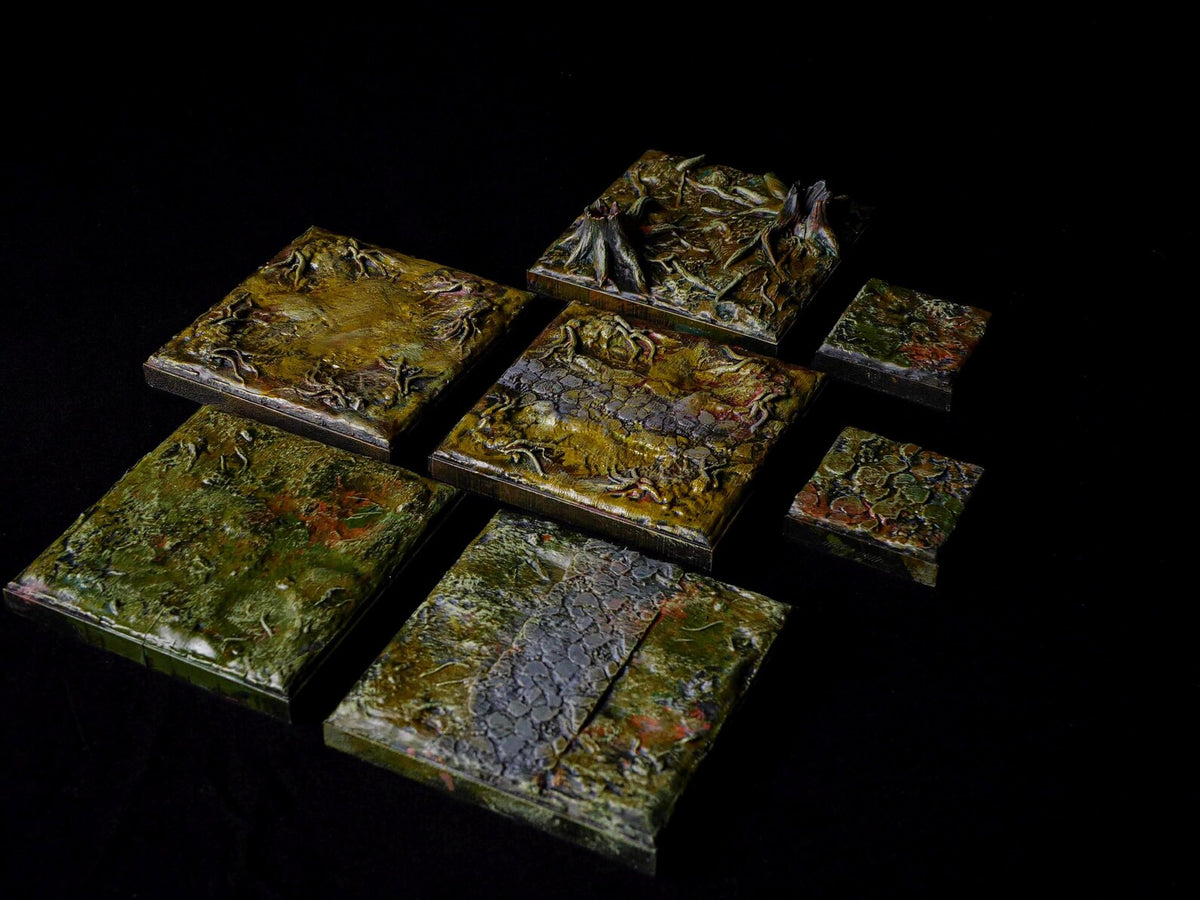 A collection of seven square and rectangular terrain tiles featuring textured surfaces in shades of green, brown, and grey. The tiles display raised details including tree stumps, root systems, and stone pathways with a glossy finish.