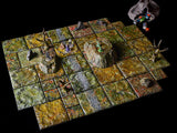 A tabletop role-playing game board composed of square, textured tiles painted in shades of green, brown, and yellow. The board features raised terrain elements, including rocky hills and bare trees, with several small character miniatures.
