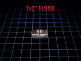 A rectangular 1x2 inch floor tile piece with a metallic silver finish and a dark, weathered, or burnt texture on the top surface. The object is positioned on a black grid background with the text 1x2 inch FLOOR printed above it.