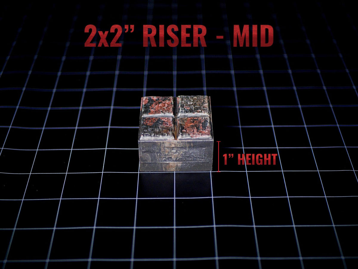 A square 2x2 inch riser with a 1 inch height, featuring a textured, weathered metallic finish with dark grey and rust-colored patches. The top surface is divided into four smaller squares, and the text 2x2 RISER - MID is visible.